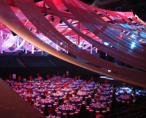 This arena was transformed into an elegant event with an intricate ceiling draping scheme and dynamic lighting that shifted through the evening for a corporate centennial celebration.