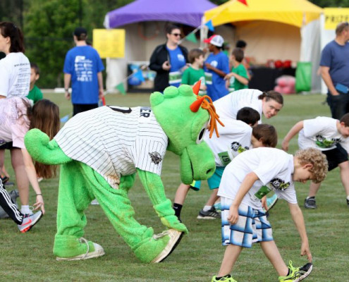 As part of a community festival, teen boys from the Let Me Run program and their coaches warming up with Charlotte Knights mascot Homer before their 5K race.