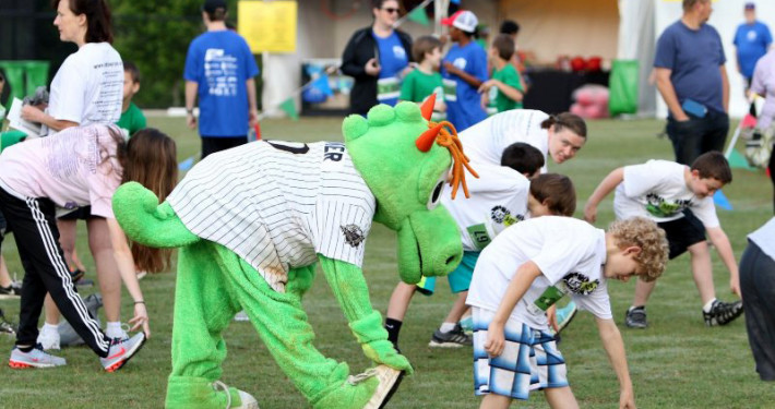 As part of a community festival, teen boys from the Let Me Run program and their coaches warming up with Charlotte Knights mascot Homer before their 5K race.